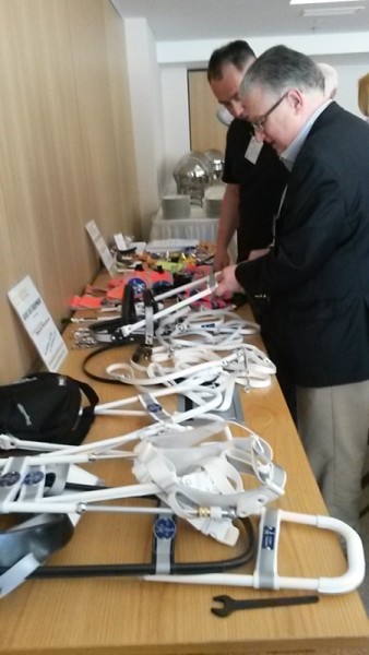 In the picture there is a variety of equipment made for guide dogs on a table next to each other. Two men are looking at them.