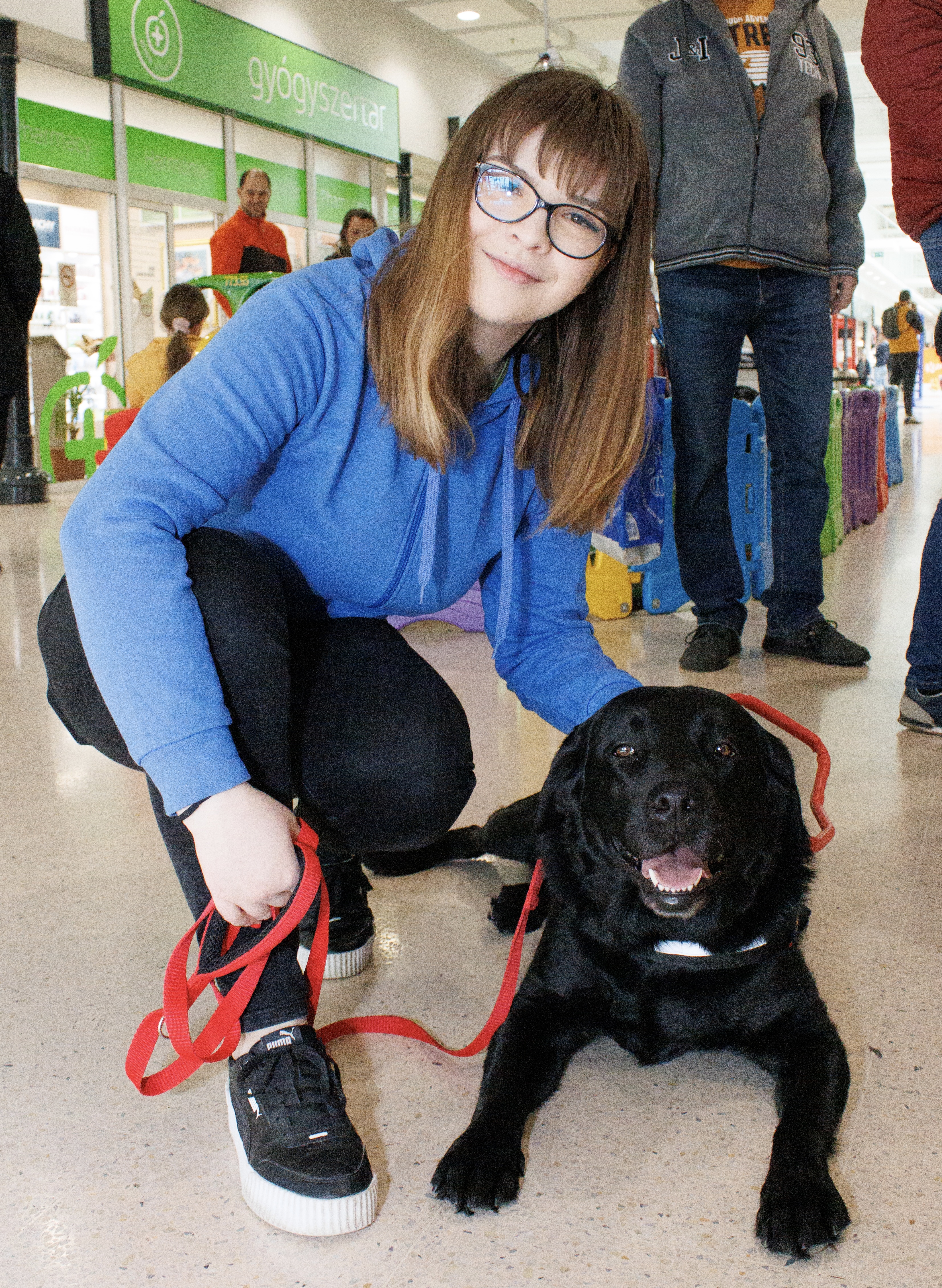 A képen Lilla guggol egy fekete vakvezető kutya, Karma mellett.