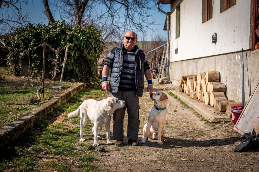 A képen Kiss Barna kliensünk látható. Mellette jobbra a nyugdíjas vakvezető kutyája Gyömbér és balra az aktív vakvezető kutyája Tangó.