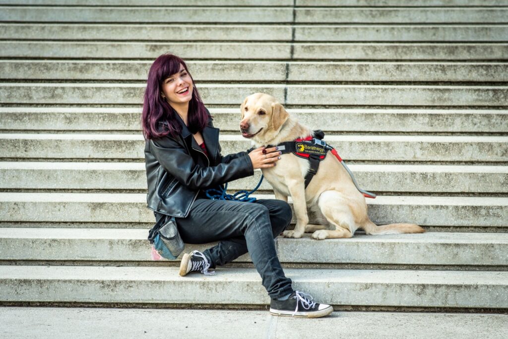 Flóra and her guide dog, Akác, are sitting at the bottom of a staircase.