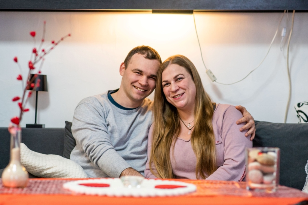 A képen Zsófi és Tamás egy kanapén ülnek, előttük egy asztal látható, miközben Tamás átöleli Zsófi vállát – meghitt, közvetlen pillanatot ábrázoló jelenet.