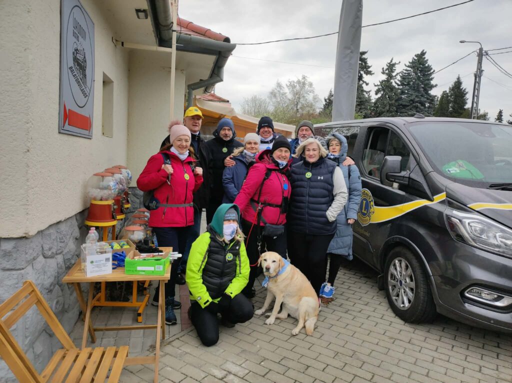 A képen a Balaton Camino útra indulók lelkes csapata látható, előttük egy sárga labrador ül.