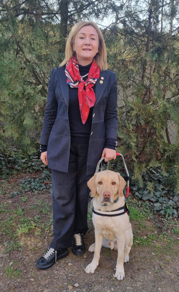 Tuncer Nurdeniz áll és mellette ül sárga labrador vakvezető kutyája Darwin