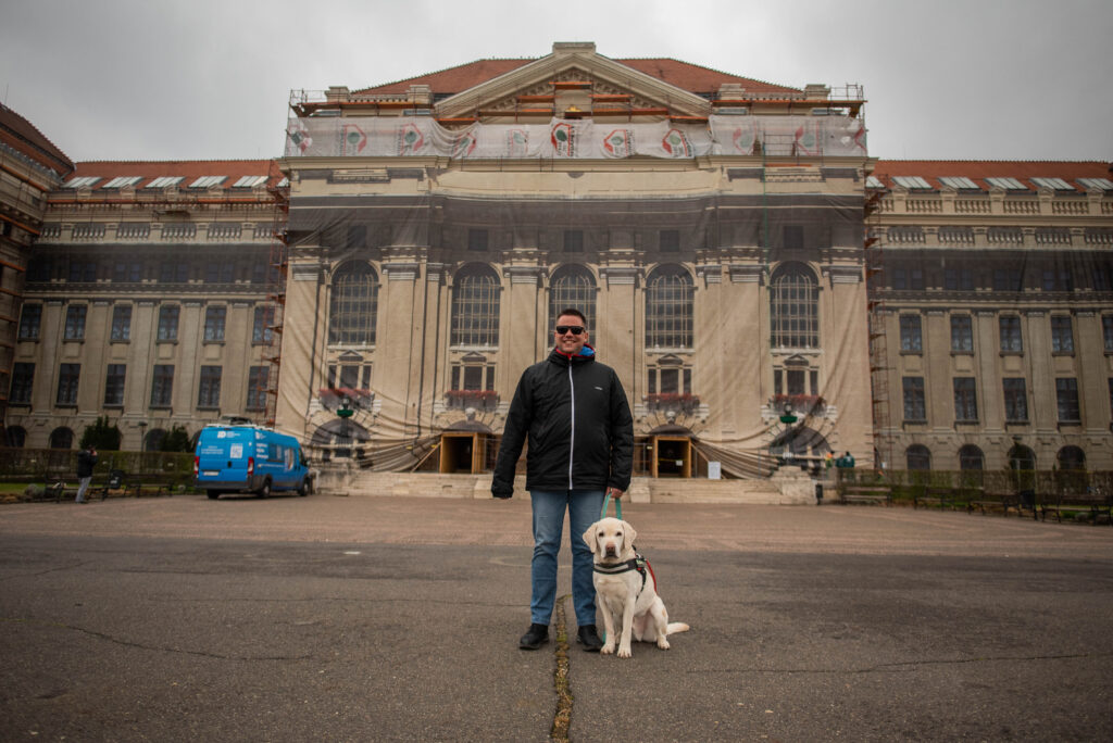 Vida Zoltán vakvezető kutyájával, Rizlinggel áll a Debreceni Egyetem főépülete előtt.