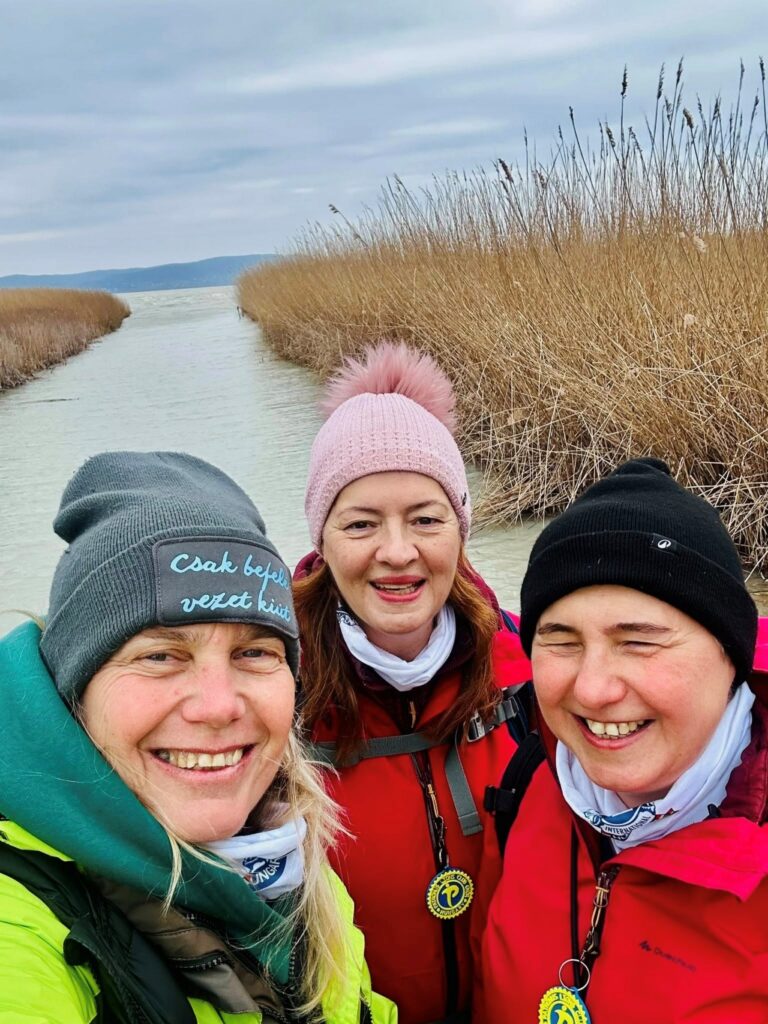 A képen három mosolygós hölgy látható, akik részt vettek a Balaton Camino nevű túrán; jobb oldalon Borsodi Erzsébet látássérült hölgy látható, mögöttük a Balaton nádasa terül el.